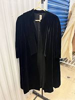 Front view of black velvet overcoat on hanger showing label and velvet panels