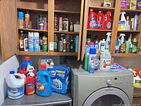 Open cabinets and washer top showing variety of cleaners, polishes, insect sprays and bleach