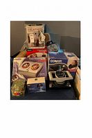 Group shot showing boxed HoMedics foot massager, boxed Conair neck massager, sealed heated wrap, HoMedics mini massager, sealed neck pillow and beige back rest