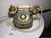Full view of ornate silver and gold tone rotary telephone on marble surface