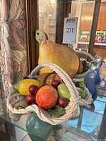 Basket with attached plastic fruit, wooden pear wall hanging and blue Krosno bottle on glass shelf