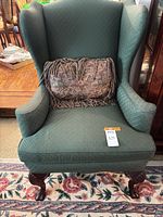 Full view of green upholstered wingback chair with pillow