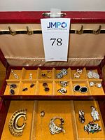 Open red jewelry box showing brooches, stick pin and overall layout