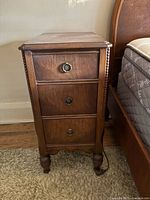 Front view of one solid oak three-drawer night table showing hardware, finish and feet