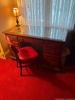 Front view of oak desk with seven drawers, glass top, matching chair, lamp