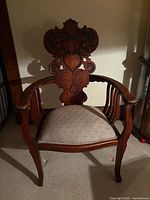 Front view of the carved oak armchair showing ornate back, curved arms, upholstered seat and general condition