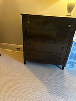 Front view of dark brown solid oak dresser showing four drawers and metal knobs