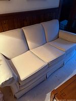 Full view of off-white three-cushion sofa with rolled arms and skirted base