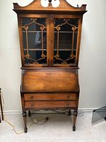 Front view of solid oak secretary desk showing glass hutch, drop-front writing surface, drawers, turned legs.