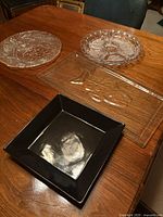 All four platters on table: two round clear pressed glass, one rectangular clear pressed glass, one square black platter