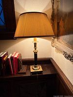 Table lamp lit, showing brass base, black column, pleated shade