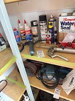 Shelf with assorted caulk, sealant cans, adhesives, caulking guns, orbital sander and sanding accessories visible