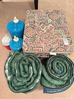 Two rolled sleeping bags, patterned foldable mattresses, two blue jugs, one red jug