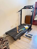 Full view of FreeSpirit treadmill with console, accessories on belt, dumbbells in bin