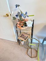 etagere with floral arrangement, vase, framed prints, hexagonal table beside