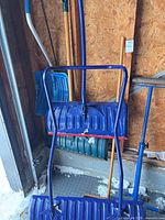 Two blue push snow shovels leaning against wall