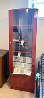 Front view of tall reddish-brown laminate audio/display cabinet with glass door and interior shelving