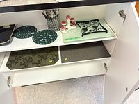 Cabinet interior showing flatware in caddy, salt & pepper shakers, square trivet on glass board, two cutting boards on lower shelf