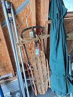 Wooden sled with rope pull next to metal poles and folded umbrella