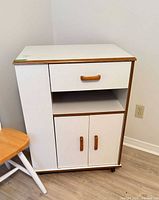 Front view of white laminate cabinet showing drawer, open shelf, double doors, casters