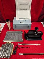 Overall lot showing stamping machine, case, manual, character rails, rods, tools, and container