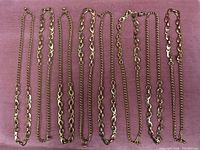 Nine gold-tone Figaro style chains laid flat on pink fabric