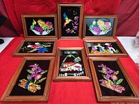 Group shot of eight framed tinsel foil reverse glass artworks on red cloth