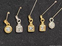 five small metal charms with stick pins through bails on black background