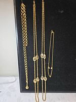 All four gold-tone necklaces hanging against black background
