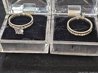 Two gold-tone solitaire rings in open acrylic boxes