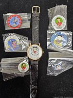 Overview of watch and six sealed discs on black background