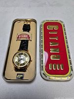 Watch in open tin case with lid alongside