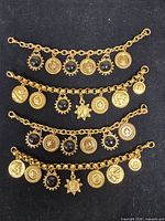 Four vintage gold-tone charm bracelets laid flat showing fronts of coin charms and cabochons