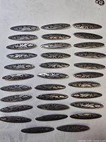 Thirty oval brooch fronts arranged in grid, showing engraved designs