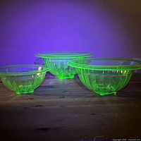 Three uranium glass bowls glowing under UV light