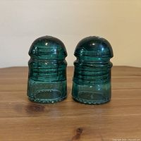 Front view of both Brookfield aqua glass insulators on wooden surface