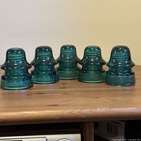 Front view of all five Brookfield aqua glass insulators aligned on tabletop