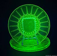 Three uranium green Depression Glass plates glowing under UV light
