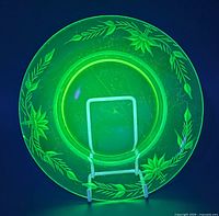 Plate under UV light showing green fluorescence and etched floral motif