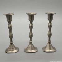 Front view of three matching silvertone metal candlestick holders standing side by side