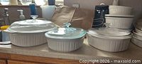 Three CorningWare dishes side by side on countertop showing size comparison and lids