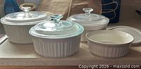 Three round casseroles with glass lids and one shallow dish shown on countertop