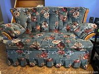 Front view of floral loveseat showing overall design, fabric pattern, wood arm trim and skirted base