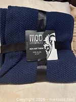 Front view of folded navy knit throw with MOD Lifestyles sleeve showing product details