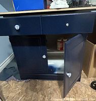 Front view of navy blue base cabinet with door open showing interior shelf and checkered knobs