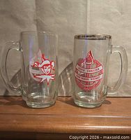 Front view of both glass beer mugs displaying respective red school graphics