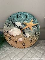 Front view of round wall clock showing beach motif dial, numerals and hands