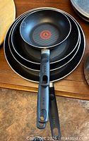 Four stacked T-fal frying pans showing handle design and interior non-stick surface