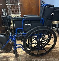 Side profile of folded wheelchair showing blue frame, armrests, rear wheels, leg rests folded