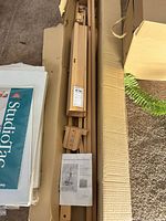 Flat-packed wooden easel components, hardware, and instruction sheet inside cardboard box